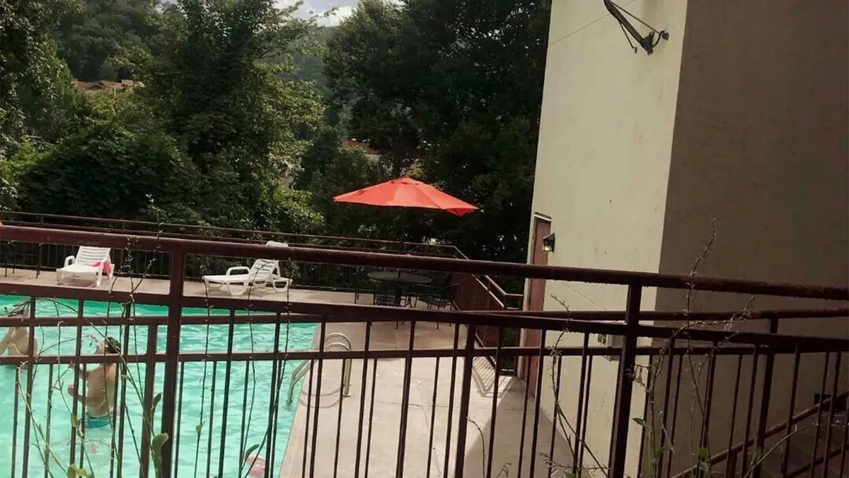 A view of a sparkling swimming pool surrounded by red umbrellas, comfortable lounge chairs, and lush green foliage, with a sense of privacy and relaxation.