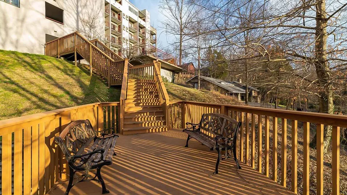The image showcases the condo's inviting wooden deck, complete with comfortable benches and a staircase leading up to it. The deck is surrounded by lush greenery, offering tranquil views and a peaceful atmosphere perfect for relaxation or small gatherings.