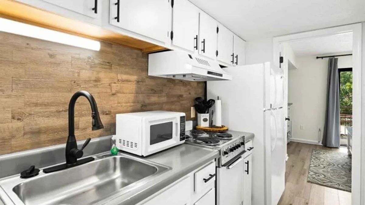 This image features a modern kitchen setup with a stainless steel sink, a sleek black faucet, a white microwave, a gas stove, and a wooden textured backsplash. The practical layout and inviting mood make it ideal for both everyday cooking and special gatherings.