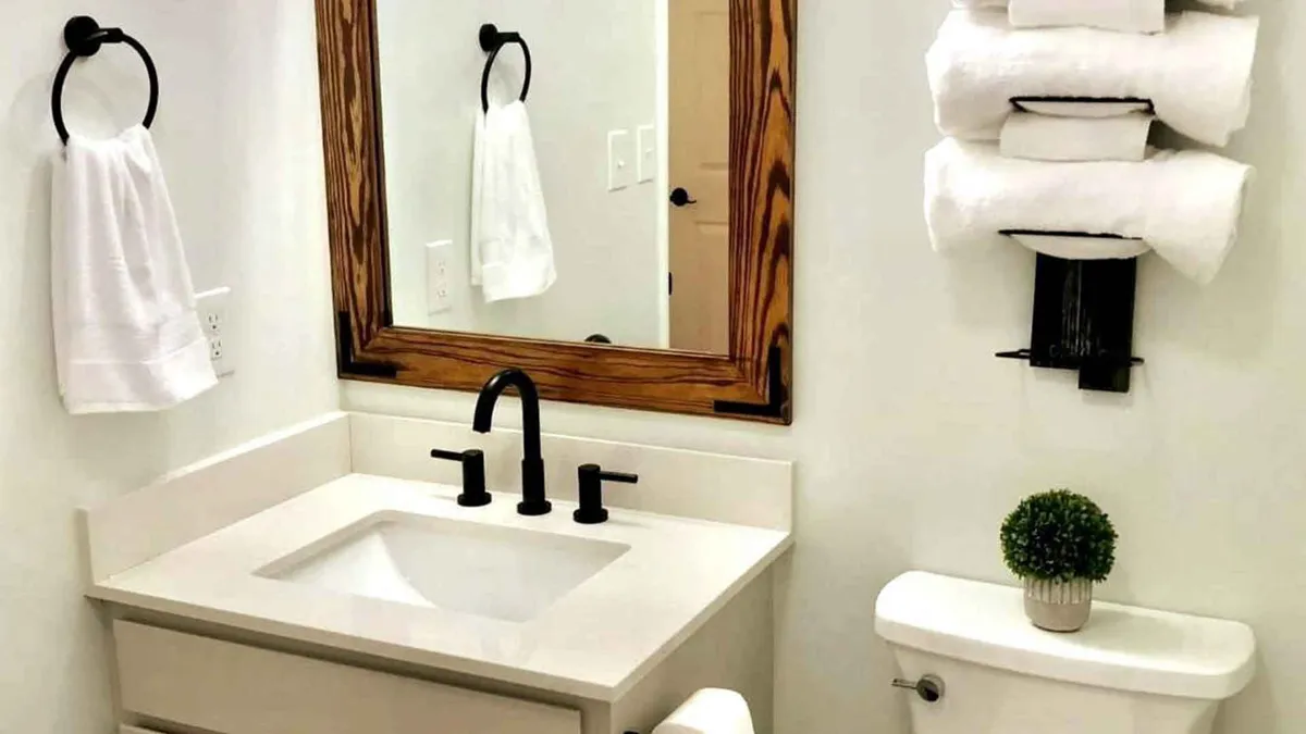 A spa-inspired bathroom vanity with a stylish wooden-framed mirror, sleek sink and faucet, neatly stacked towels, and a small potted plant for a touch of nature. The space feels calm, inviting, and fresh, ideal for personal care and relaxation.