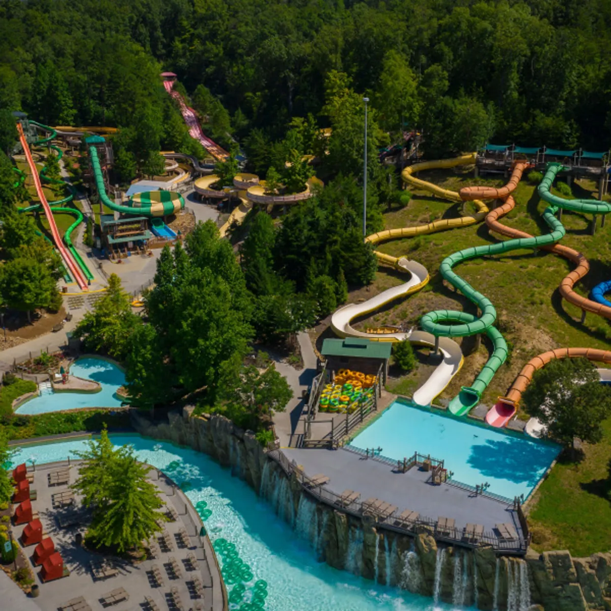 This vibrant exterior image showcases a pool complex with water slides, shimmering swimming pools, lush greenery, and decorative waterfalls. Families can be seen enjoying themselves by the pool, embodying fun, relaxation, and togetherness.
